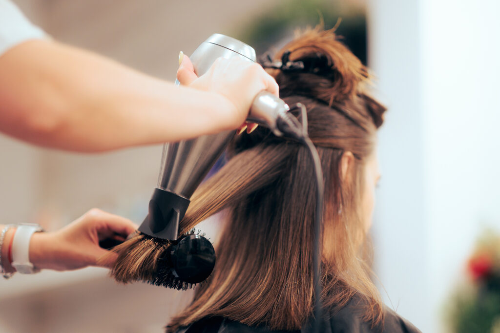 Stylist using a blow dryer and round brush during a professional blowout service in a modern beauty studio.